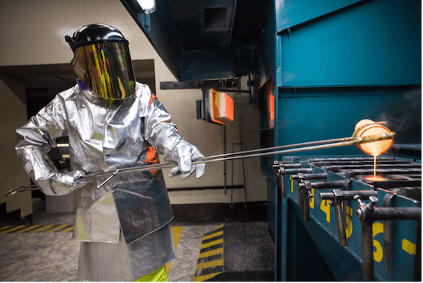 Person with PPE holding a vial with molten liquid and pouring it into a container