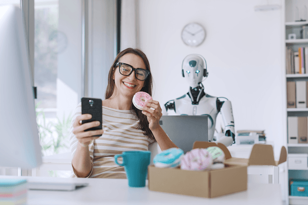 Woman holding a donut while looking at her phone smiling, with a robot in the background staring menacingly at the woman