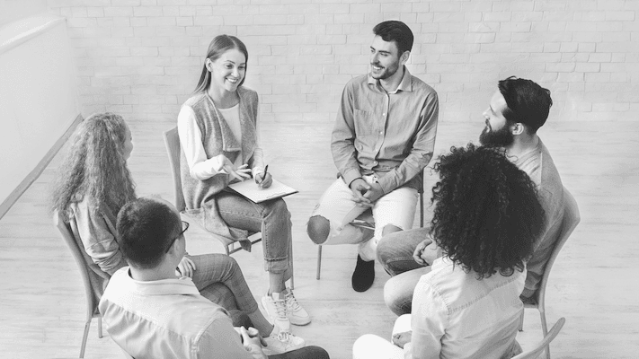 A group of people sitting in a circle smiling and talking | Featured Image for the National Safety and Quality Mental Health Standards for Community Managed Organisations service page