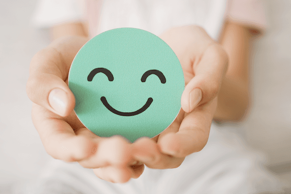 Person holding a teal circle with a smiling face