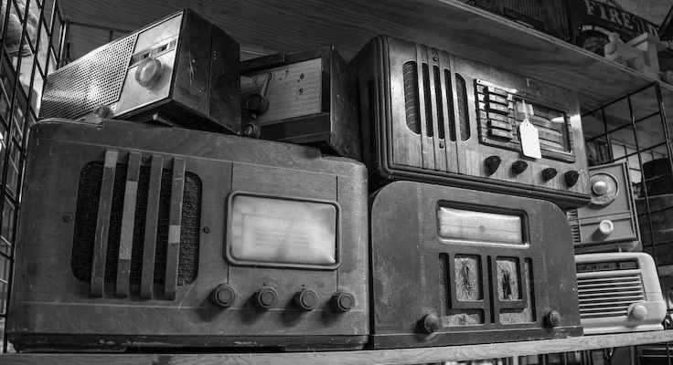 A bunch of older style radios on a storage bench