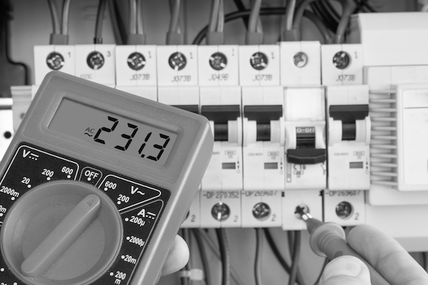 Someone holding a voltmeter to a breaker board, with the screen of the device visible