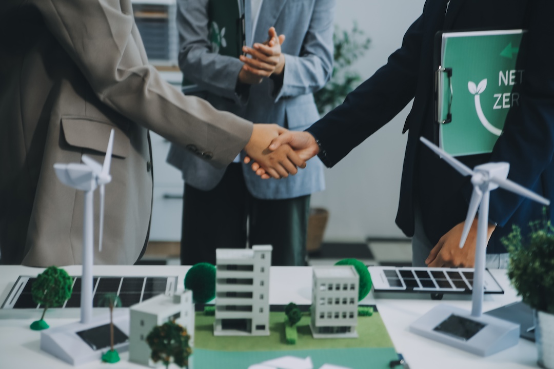 Two people handshaking with person on right holding clipboard with Net Zero label