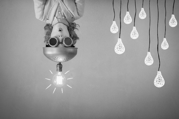 Upside down girl wearing a make-shift hat with a lightbulb attached next to other lightbulbs on strings