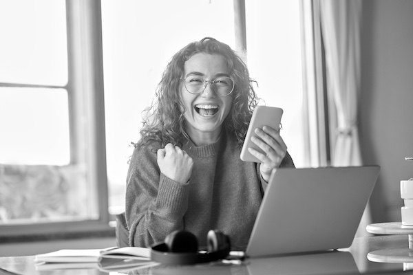 Woman smiling with phone in hand sitting in front of laptop